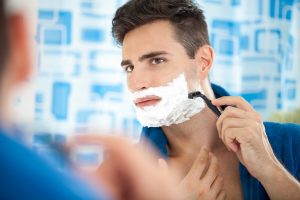 Close up of a young man shaving using a razor